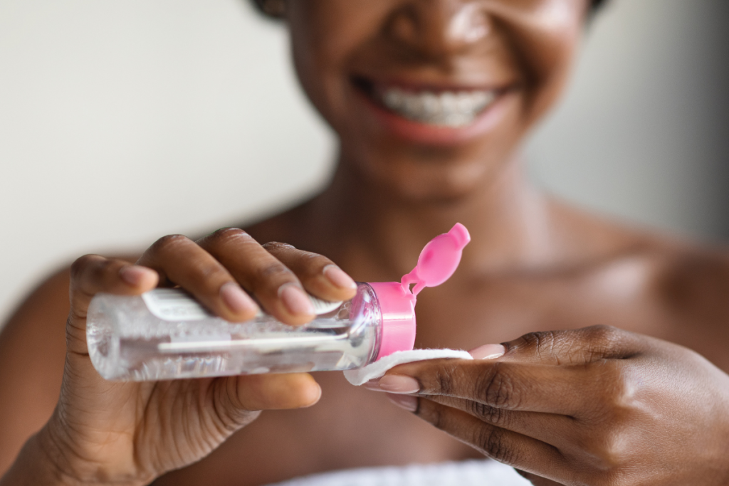 A woman applying micellar water to a pad for makeup removal